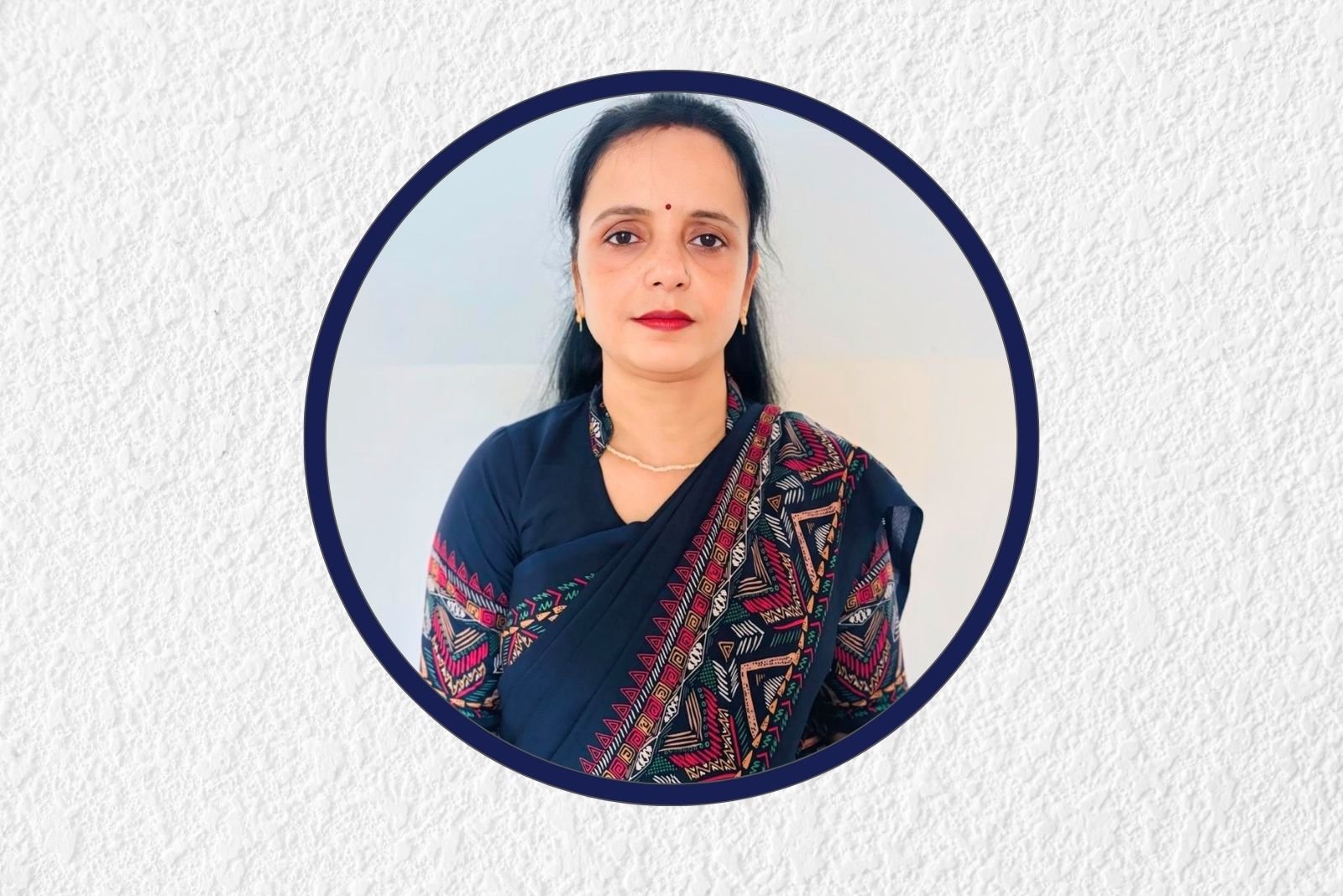 Portrait of a woman in a navy blue saree with geometric red and pink patterns, centered in a circular navy frame on a textured white background.