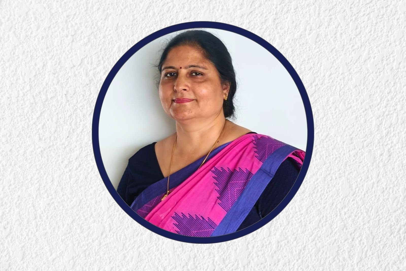 Portrait of a woman in a pink and purple saree, inside a circular navy frame on a light textured background.