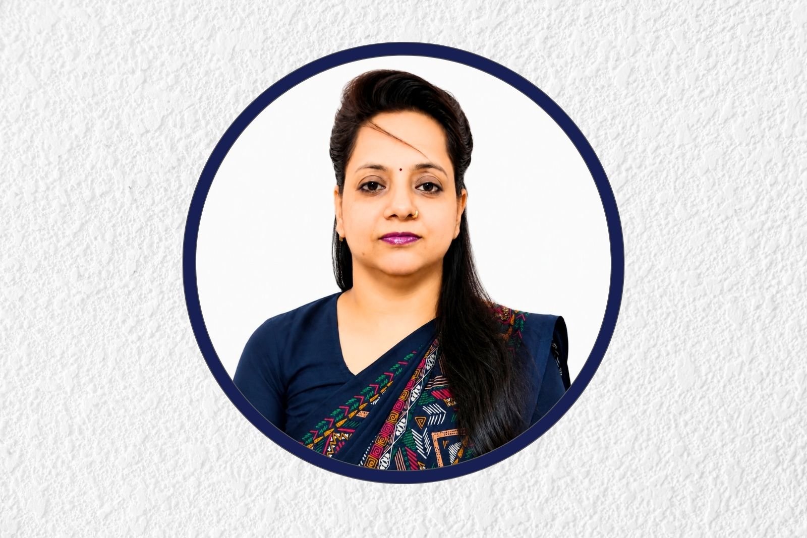 Head-and-shoulders portrait of a woman in a navy saree with a bindi, framed by a dark blue circular border on a textured gray background.