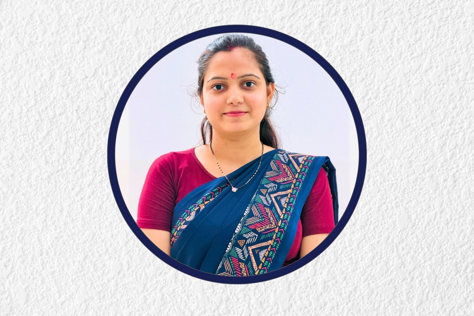 Portrait of a smiling woman in a maroon blouse and blue patterned sari, framed by a dark blue circular border on a light background.